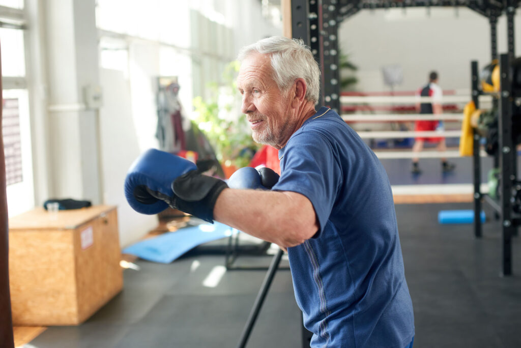 Senior man beats punching bag in gym.